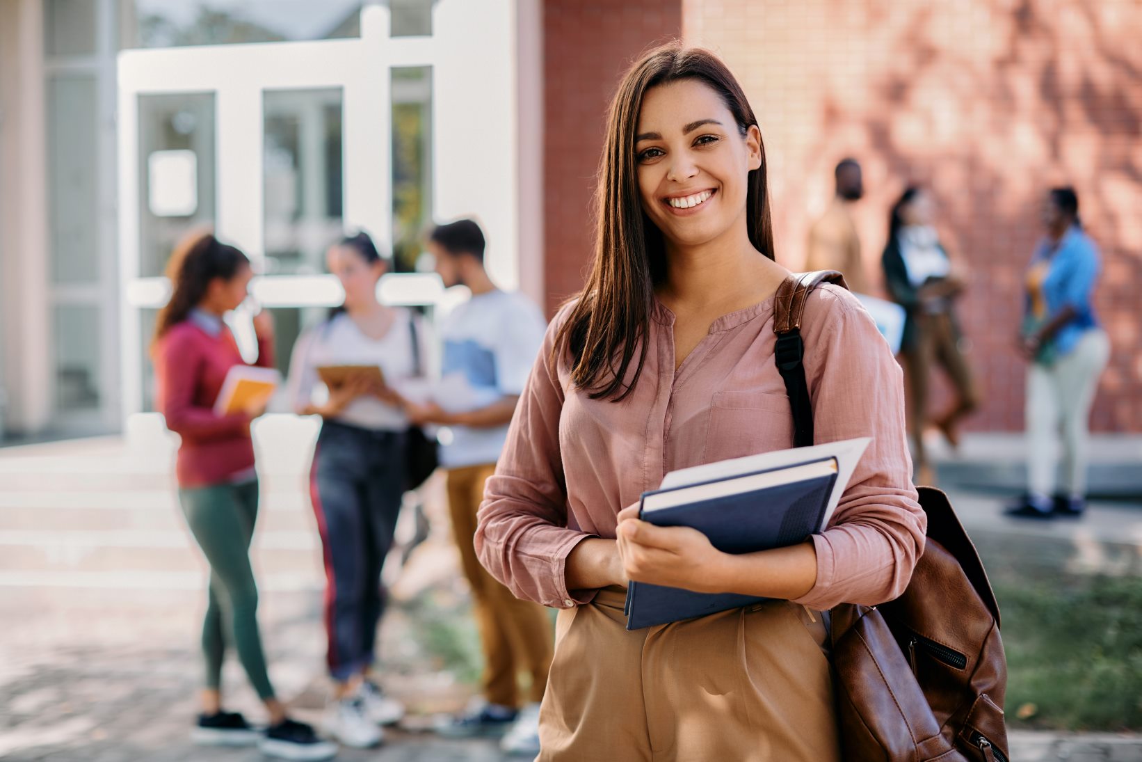 Women carrying books, on a college campus, with other students around