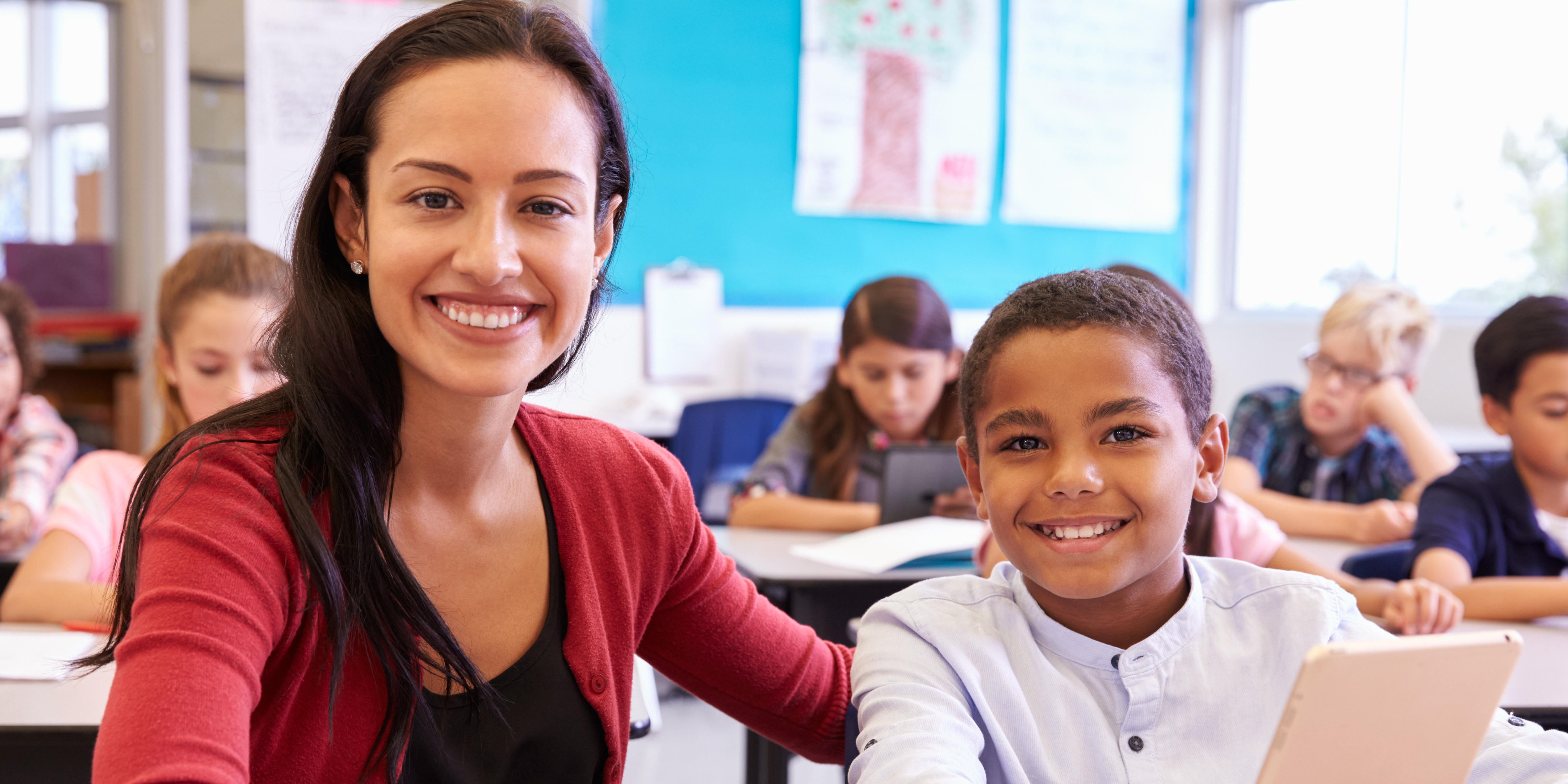 Portrait of teacher with elementary school boy at his desk
